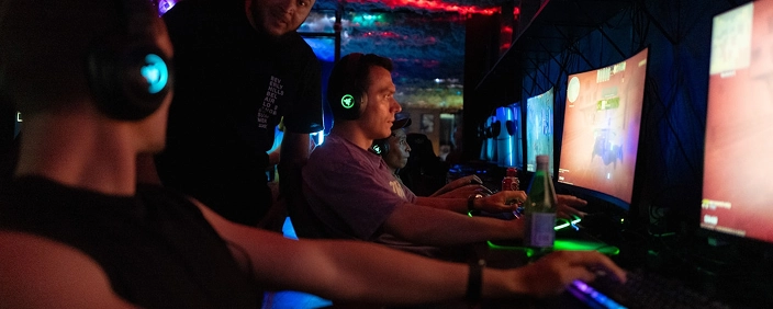 Professionele esports-spelers zitten aan verlichte gamingstations in een moderne offline cyberclub, voorzien van headsets en geconcentreerd op competitieve multiplayer-gameplay die wordt weergegeven op grote monitoren, met RGB-toetsenborden en een sfeer van donkere neonverlichting die kenmerkend is voor teamtrainingen
