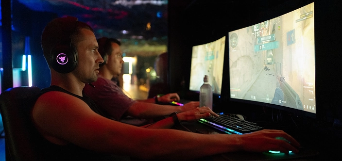 Competitief gamingteam dat samen traint op krachtige pc-opstellingen in een esports-club, terwijl een coach de gameplay van achteren begeleidt, waarbij de nadruk ligt op teamwork, strategieontwikkeling en gestructureerde trainingsomstandigheden in een professionele offline cyberclub met kleurrijke ledverlichting.